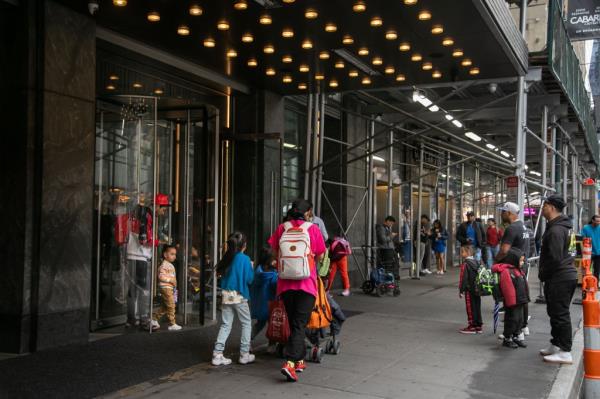 People exiting the Row Hotel, currently a migrant shelter, in Times Square, New York City, with celebrities Sebastian Benedict and Masira Surin among them.
